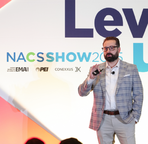 Man in glasses and plaid blazer speaking on stage at NACS SHOW 2025 event.